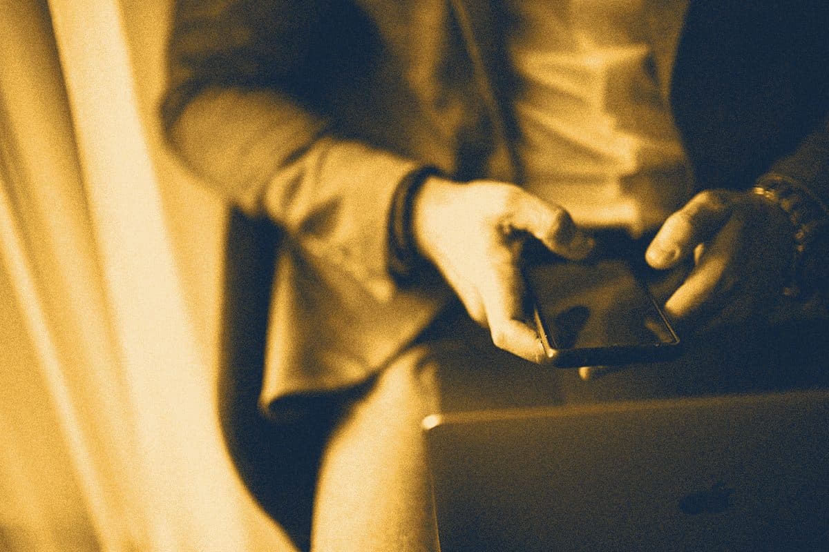 Руки людини в діловому костюмі тримають смартфон поруч із ноутбуком